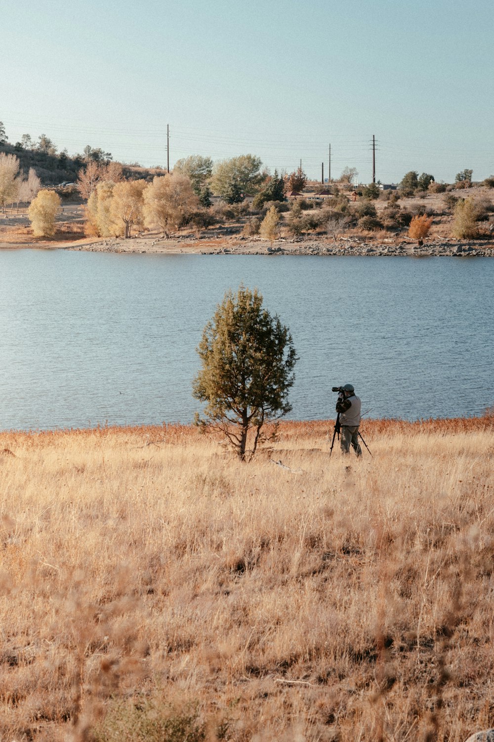 person in black jacket standing on brown grass field near body of water during daytime