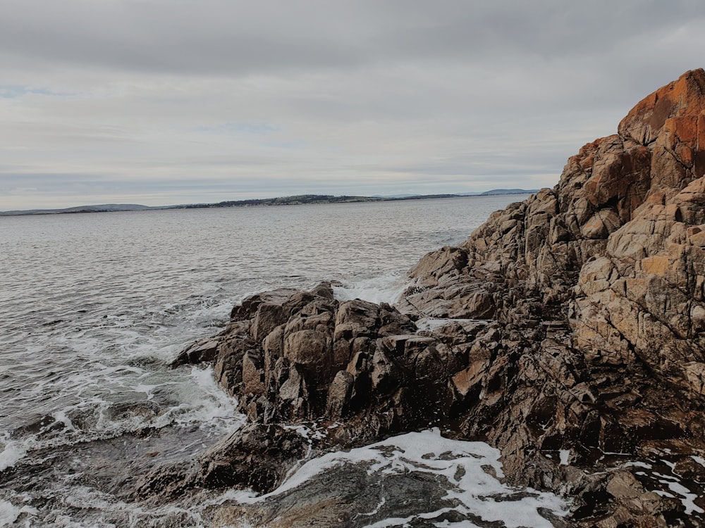 brown rock formation on sea under white clouds during daytime