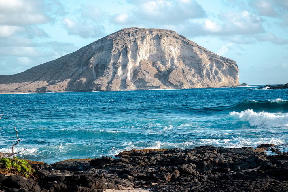 brown and green mountain beside blue sea under blue sky during daytime