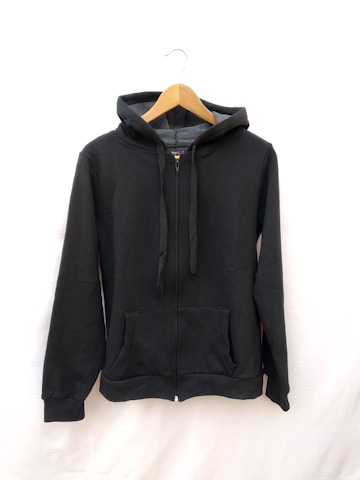 A black hoodie is displayed on a wooden hanger. The hoodie has a zipper in the front, two front pockets, and drawstrings for the hood. The background is plain white.