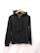 A black hoodie is displayed on a wooden hanger. The hoodie has a zipper in the front, two front pockets, and drawstrings for the hood. The background is plain white.