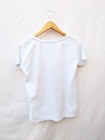 A plain white t-shirt is displayed on a wooden hanger against a light background. The t-shirt is short-sleeved and appears to be made of a lightweight material.