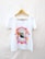 A white t-shirt hanging on a wooden hanger features a graphic design. The center showcases an eagle's head within a star shape, surrounded by flames and text that reads 'Rock and Roll' and 'Made in Heaven.'