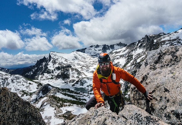 A climber wearing Telsfa gloves and knee pads scaling a rocky mountain trail at sunrise.