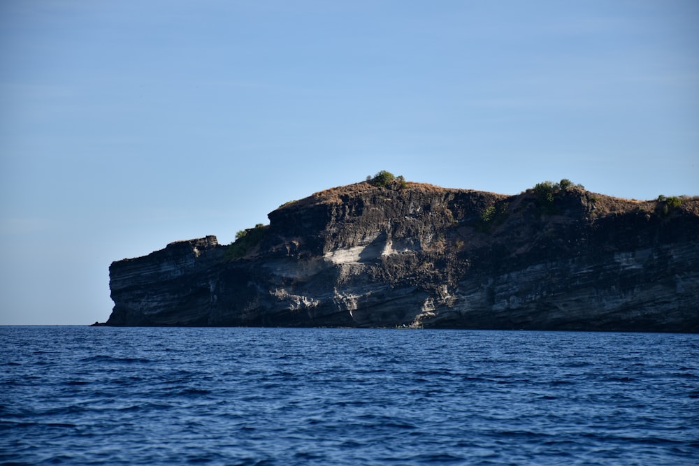 green and brown mountain beside sea under blue sky during daytime