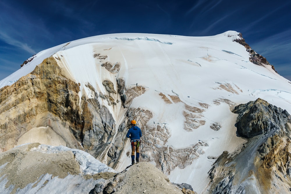 man in blue jacket and black pants standing on snow covered mountain during daytime