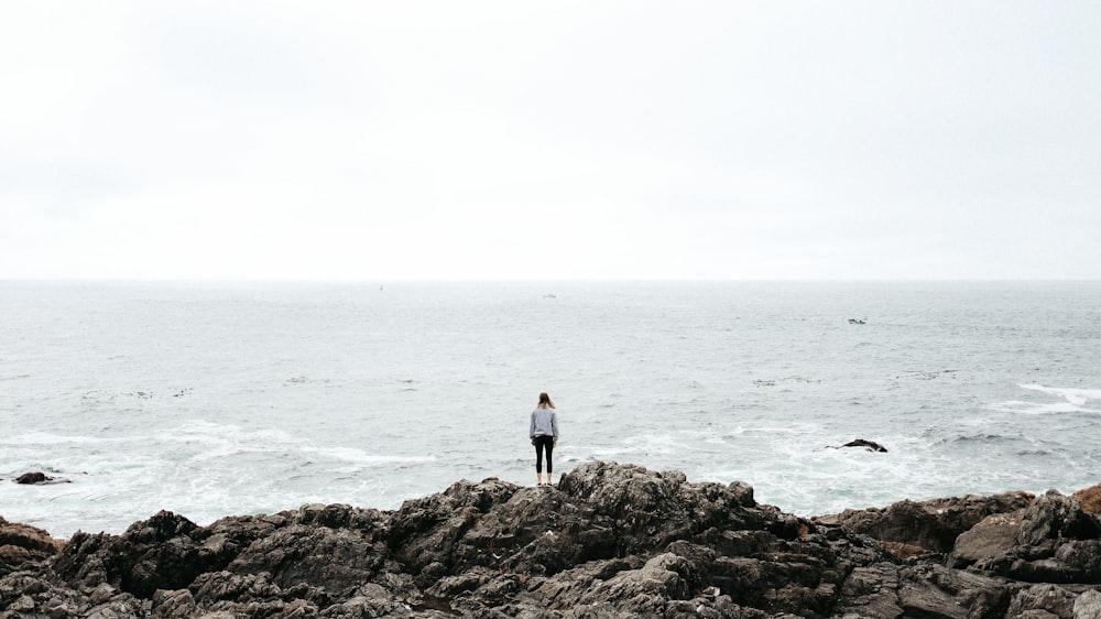 man in white shirt standing on rock near sea during daytime