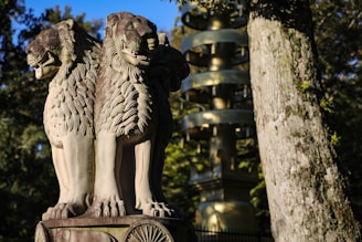 A detailed sculpture of three lion heads with ornate manes stands prominently. The background features a tall golden pagoda and lush green trees, highlighting a serene outdoor setting.