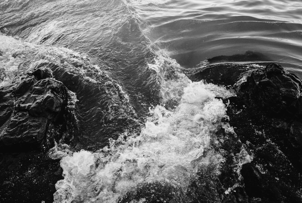 water waves hitting rocks in grayscale photography