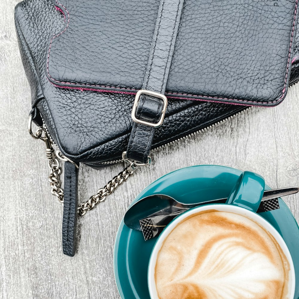 black leather sling bag beside blue ceramic mug with coffee
