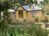 A charming Caribbean-style house with a bright yellow facade and lush tropical garden.