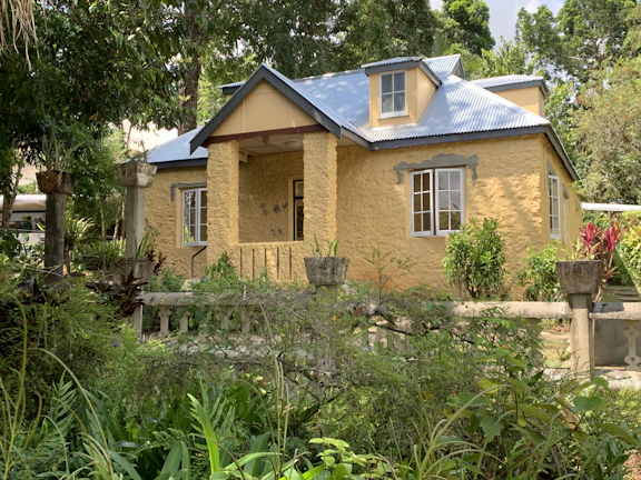 A charming Caribbean-style house with a bright yellow facade and lush tropical garden.