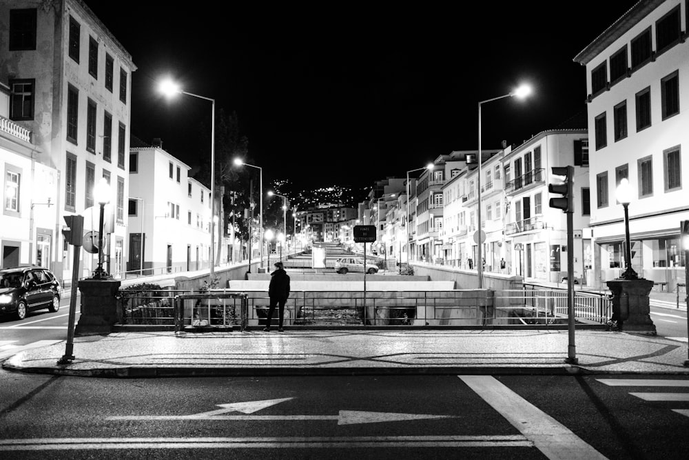 grayscale photo of man walking on sidewalk