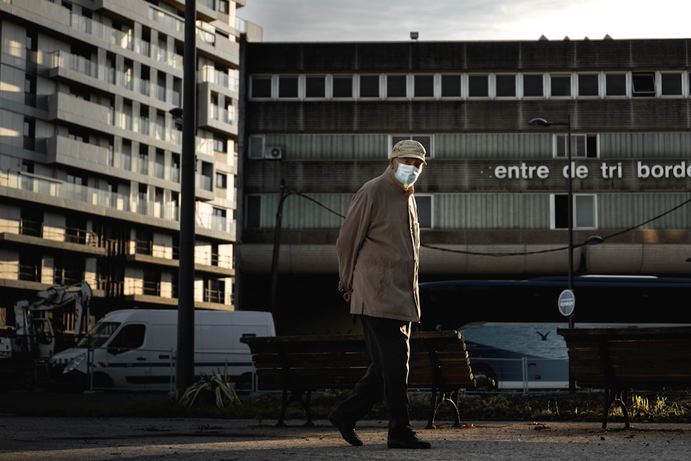 man in brown coat standing near blue and white bus during daytime