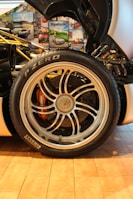 A detailed close-up of a car's wheel and tire is surrounded by various automotive-themed posters. The tire is branded Pirelli P Zero, and the alloy wheel features intricate spoke designs with visible brake components underneath.