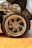 A detailed close-up of a car's wheel and tire is surrounded by various automotive-themed posters. The tire is branded Pirelli P Zero, and the alloy wheel features intricate spoke designs with visible brake components underneath.