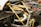 A close-up view of a car's engine compartment showcasing its intricate design and engineering. The image highlights carbon fiber components, metallic structures, and a yellow cover over part of the engine. Various automotive magazines, including titles like Top Gear and Autocar, form the background.