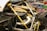 A close-up view of a car's engine compartment showcasing its intricate design and engineering. The image highlights carbon fiber components, metallic structures, and a yellow cover over part of the engine. Various automotive magazines, including titles like Top Gear and Autocar, form the background.