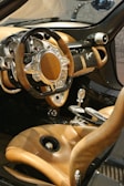A luxurious car interior featuring a steering wheel with a unique design, incorporating both wood and metallic elements. The dashboard is equipped with multiple gauges and displays, adding a sense of sophistication. The seats are upholstered in high-quality tan leather, complementing the overall elegant look. The gear shift and other controls are crafted with precision, contributing to the opulent feel of the vehicle.