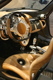 A luxurious car interior featuring a steering wheel with a unique design, incorporating both wood and metallic elements. The dashboard is equipped with multiple gauges and displays, adding a sense of sophistication. The seats are upholstered in high-quality tan leather, complementing the overall elegant look. The gear shift and other controls are crafted with precision, contributing to the opulent feel of the vehicle.