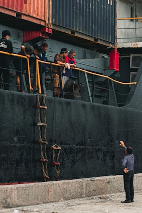 man in gray t-shirt and black pants standing beside black metal fence during daytime