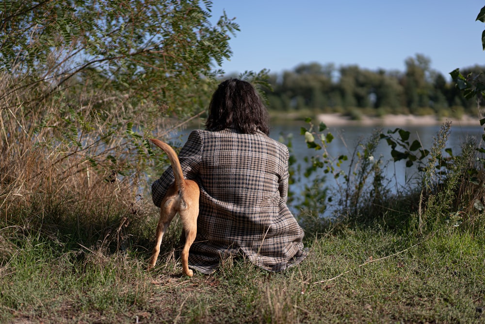 woman in white and black plaid dress shirt holding brown short coated dog on green grass