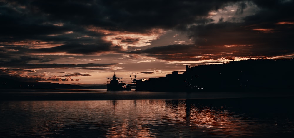 silhouette of building near body of water during sunset