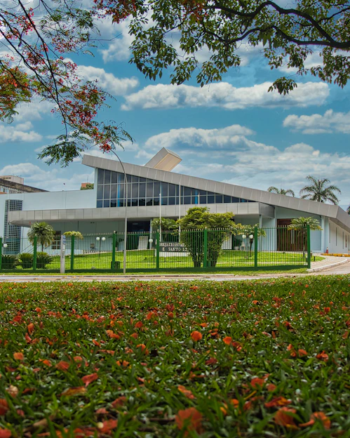A modern architectural building with clean lines surrounded by greenery under a bright sky.