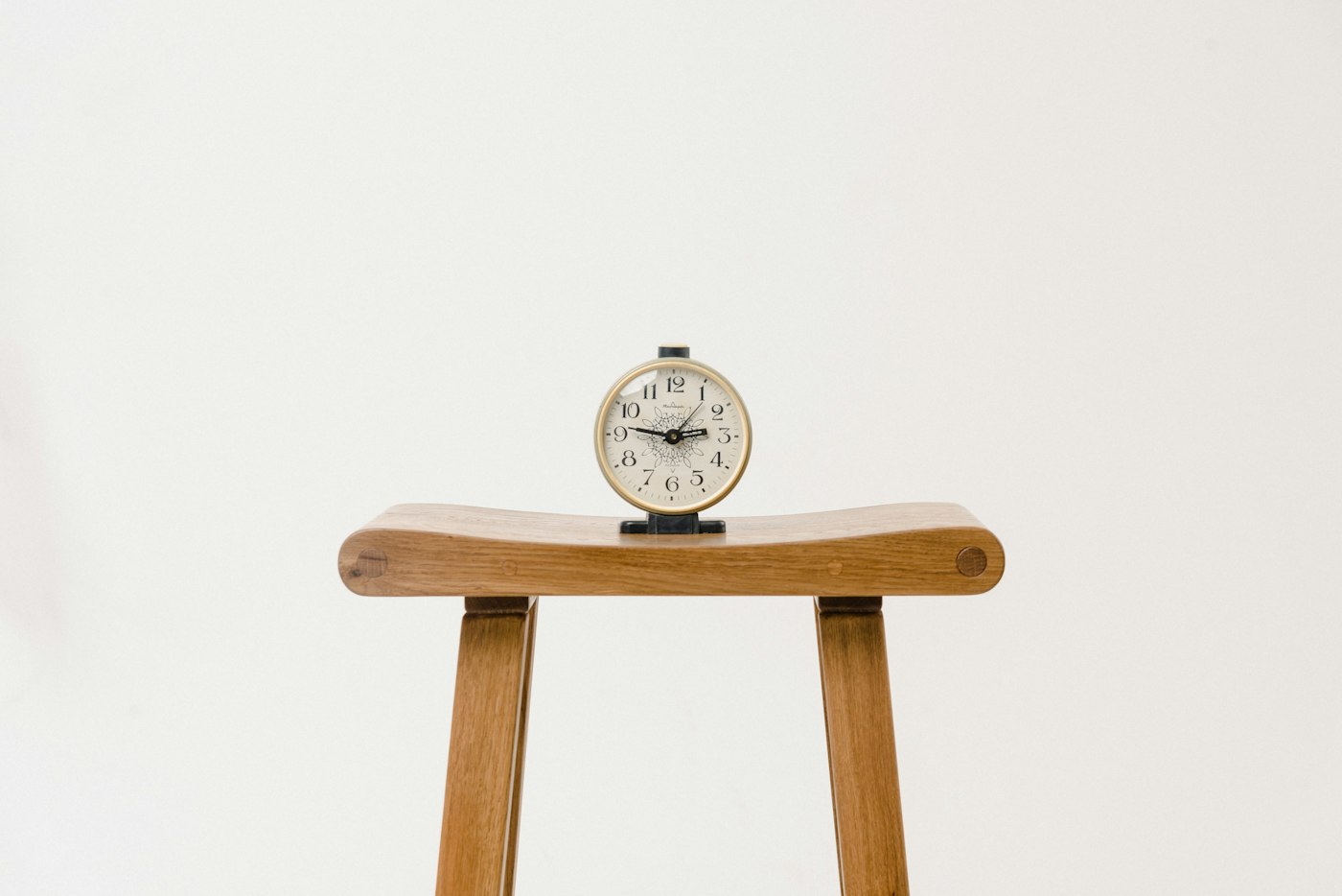 Small wooden clock on a stool against a white wall