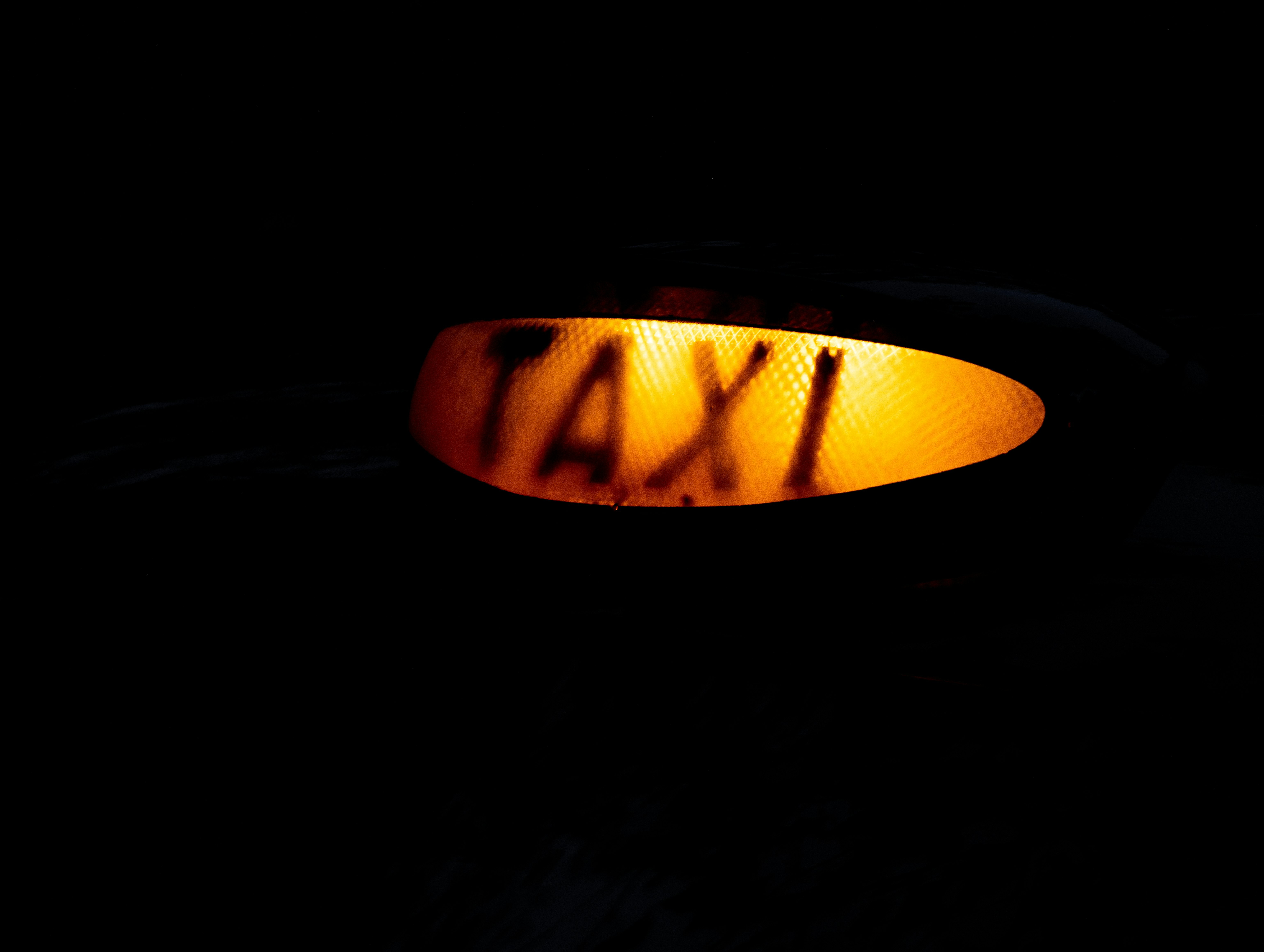 Illuminated orange London taxi sign, isolated on a black background.