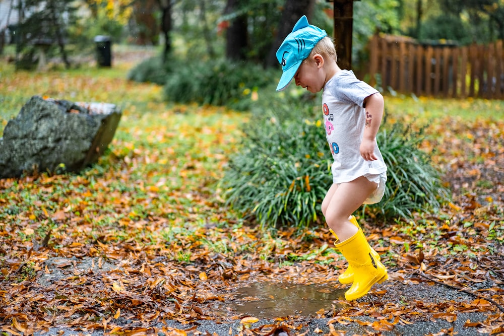 fille en chemise blanche et pantalon jaune courant sur des feuilles séchées brunes pendant la journée