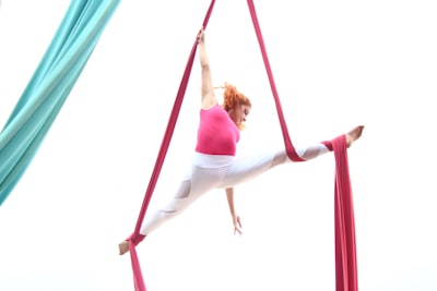 woman in pink tank top and white pants hanging on red hammock bow teams background