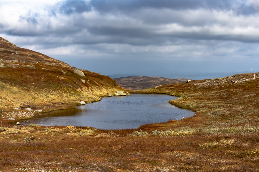 montagna marrone e verde accanto allo specchio d'acqua sotto il cielo nuvoloso durante il giorno