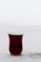 A glass filled with a dark red liquid is placed on a textured, light-colored surface. The surroundings are minimalistic and serene, with an overcast or foggy background that gives a muted, soft appearance.