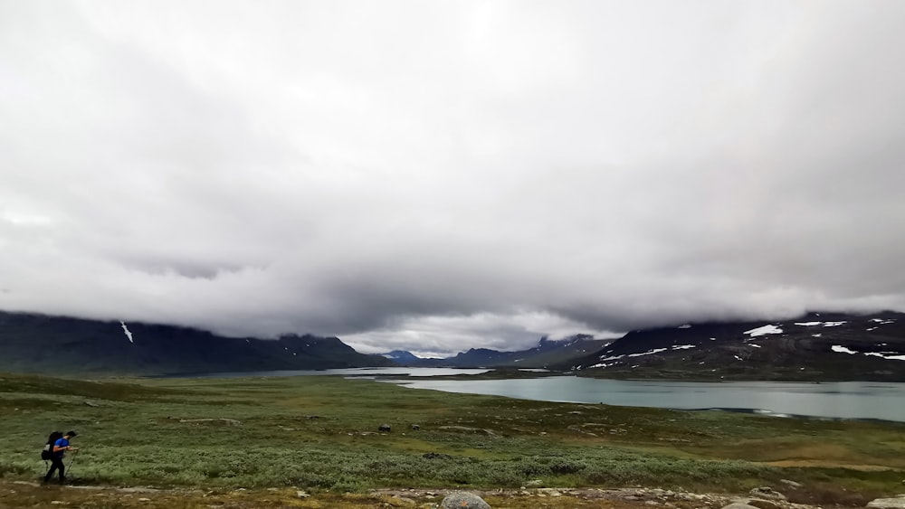 green grass field near body of water under white clouds during daytime