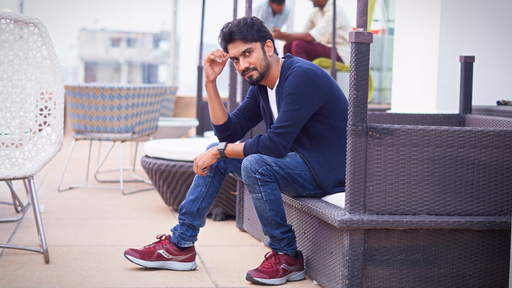 man in blue long sleeve shirt and blue denim jeans sitting on gray concrete bench during