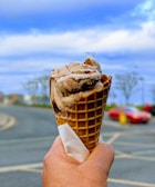 Close-up of a vibrant berry and chocolate swirl ice cream cone held against a sunny park background.