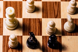 A close-up view of a chessboard with wooden squares, featuring both black and white chess pieces in play. The board showcases a variety of chess pieces, including pawns and knights, indicating a game in progress.