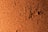 A textured surface of brown cork material, featuring an irregular, rough pattern with scattered dark indentations.