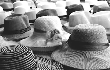 A collection of hats in various styles and patterns is displayed, featuring both light and dark shades. The intricate designs of the hats include woven textures and ribbon embellishments, creating an array of visual interest.