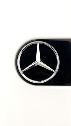 A shiny, silver, three-pointed star emblem set against a black circular background. The emblem is centered and surrounded by a thin chrome ring, with a clean white backdrop filling the rest of the image.