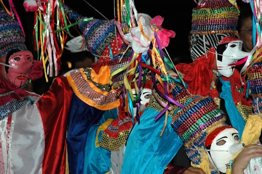 Colorful, sequined costumes and masks create a vibrant and festive scene, with bright ribbons and intricate patterns. The costumes are adorned with various textures and details.