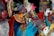 Colorful, sequined costumes and masks create a vibrant and festive scene, with bright ribbons and intricate patterns. The costumes are adorned with various textures and details.