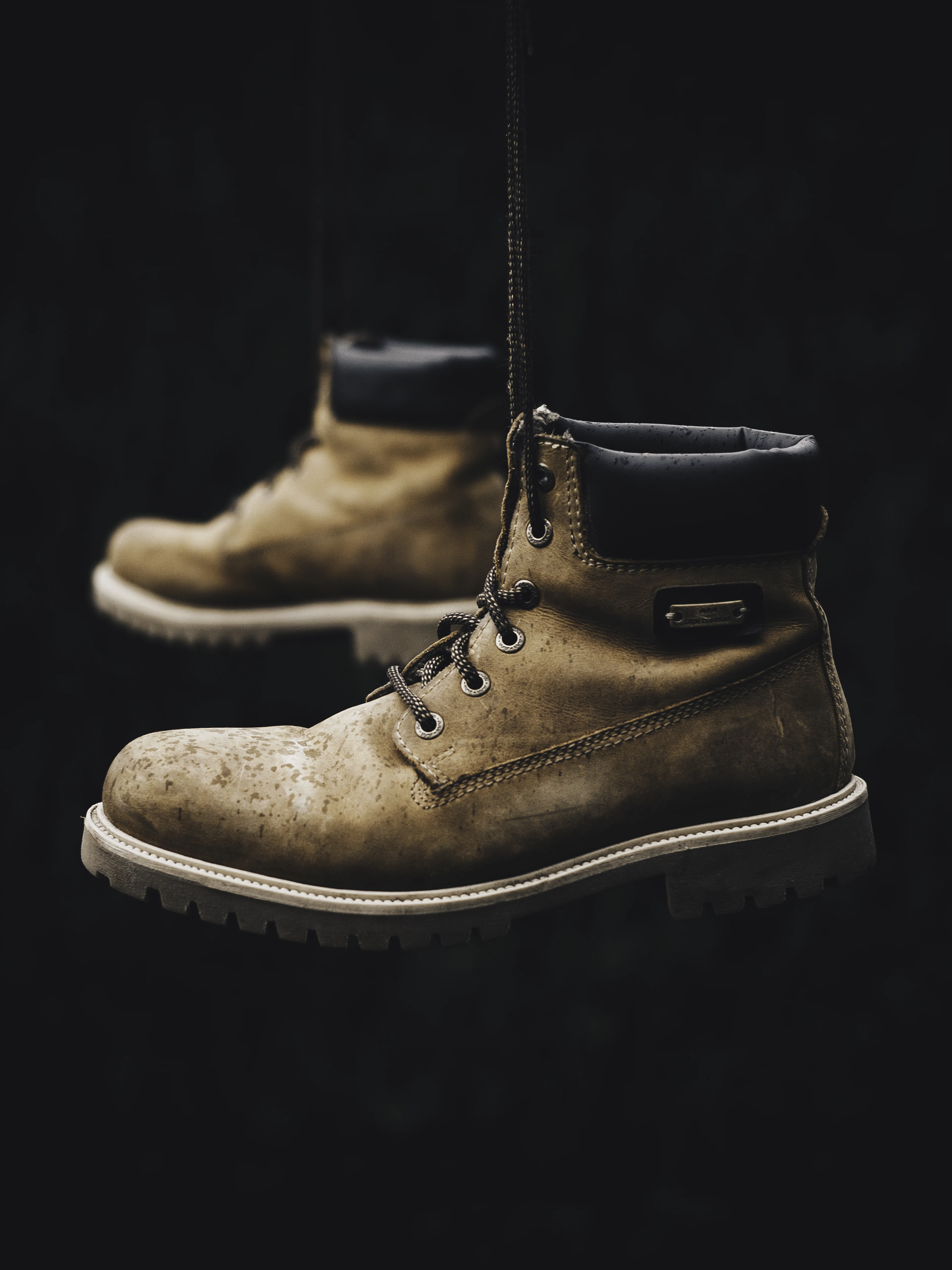 A pair of worn hiking boots suspended against black