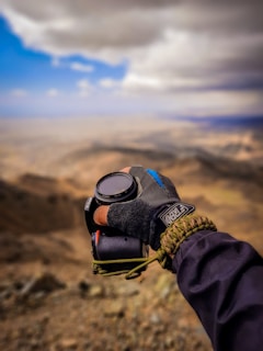 Close-up of a hand holding a branded outdoor gear product with mountains in the background