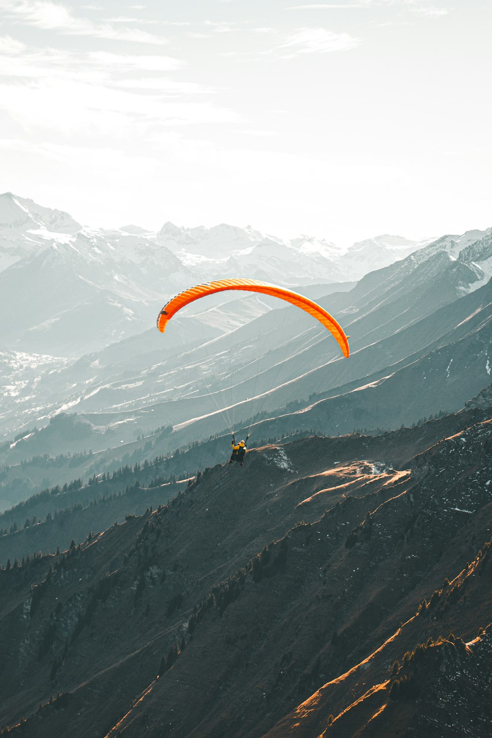 person in yellow parachute over snow covered mountains during daytime