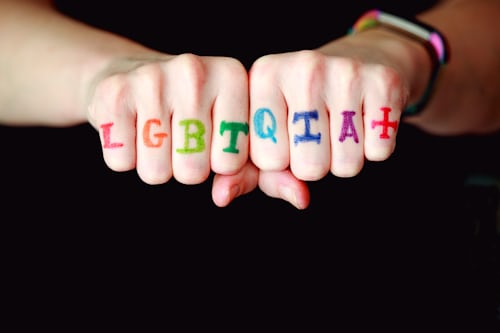 Two fists side by side with LGBTQIA+ written in rainbow colours across the knuckles.