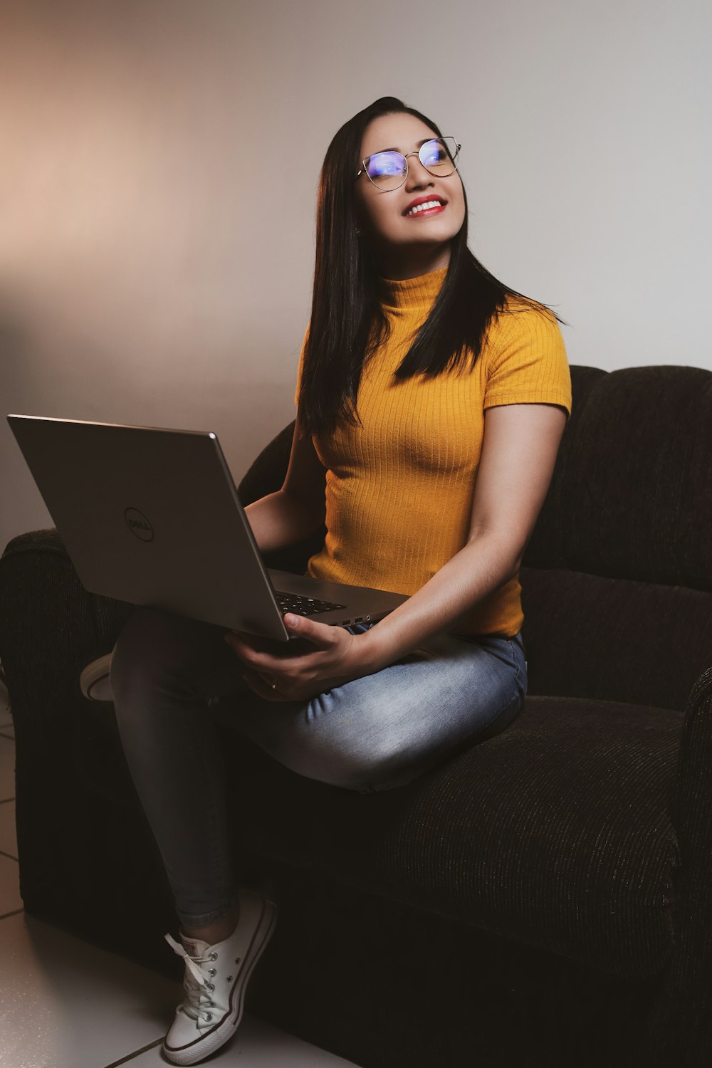 woman in yellow shirt and blue denim jeans sitting on gray sofa using macbook