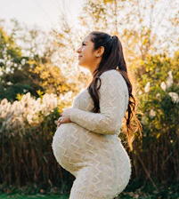 Pregnant woman smiling outdoors, radiating calm and happiness in natural light.