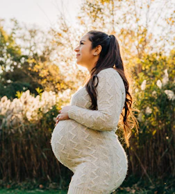 Pregnant woman smiling outdoors, radiating calm and happiness in natural light.